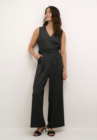 Jumpsuit nero senza maniche con scollatura a V, bottoni frontali, vita con cintura e pantaloni a gamba larga. Tessuto liscio con una texture leggera.