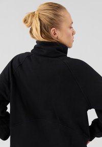 Must musta dressipluus kõrge krae, raglaanvarrukate ja tekstuurse kangaga. Seljal läbib õmblusdetail ja lõike lõdvestatud.