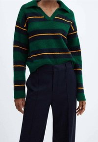Zielony sweter w poziome paski w kolorach granatowym i pomarańczowym zestawiony z granatowymi spodniami w pionowe paski z wysokim stanem na osobie.