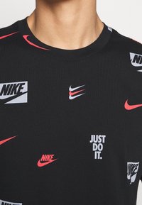 Svart bomulls-t-shirt med olika Nike-logotyper i rött och vitt. Designen inkluderar texten "JUST DO IT", rund halsringning och korta ärmar.