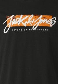 T-shirt nera con grafica audace in bianco e arancione che riporta il testo "Jack & Jones" e "FUTURE O IL TUO FUTURO". Materiale in cotone morbido.