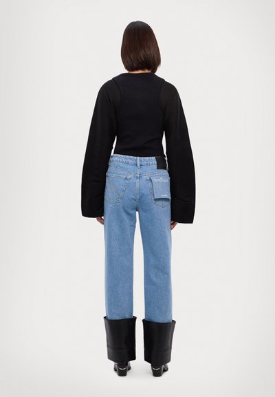 Zwart langarm top met een getailleerde pasvorm en wijde mouwen, gecombineerd met lichtblauwe rechtlopende jeans en zwarte plateau boots.