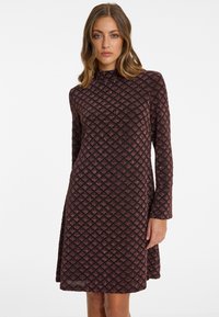 Long-sleeve dress in dark maroon with a textured diamond pattern, featuring a high neckline and a flared hemline. Made of soft stretch material.