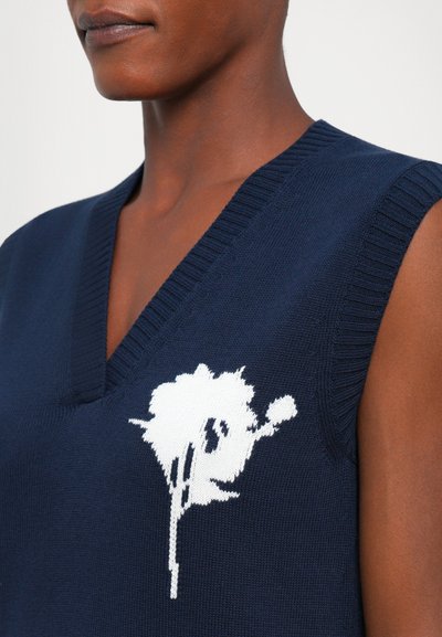 Marineblå ermeløs genser med dyp v-hals, med et hvitt blomstermønster på brystet. Strikket tekstur med ribbede kanter.