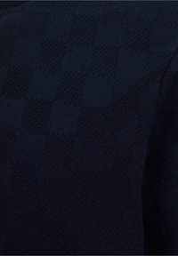 Dark blue fabric with a textured checkerboard pattern of alternating smooth and raised knit squares.