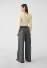 Sweter w kolorze off-white z warkoczowym splotem i szerokim dekoltem, zestawiony z wysokim stanem szarymi spodniami o szerokich nogawkach. Spodnie posiadają tylne kieszenie i detale w postaci guzików.