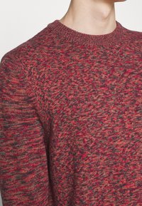 Maglione lavorato a maglia nelle tonalità di rosso e grigio, con un design a girocollo caratterizzato da un motivo testurizzato e polsini a coste.