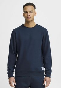Mornarsko modra majica s crewneck iz mešanice mehke bombažne tkanine z rebrastimi manšetami in robom, s poudarjeno majhno etiketo na spodnji strani.