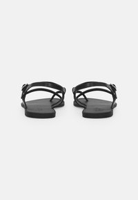 Black flat sandals featuring multiple intertwined straps and an adjustable buckle. Smooth texture with a minimalist design.