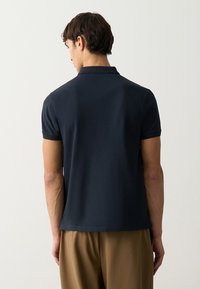 Polo shirt navy con maniche corte, texture liscia e colletto classico. La parte posteriore presenta un design minimalista senza loghi o accenti visibili.
