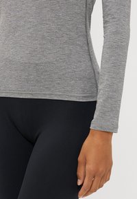 Maglietta grigia a maniche lunghe con sottili righe, dotata di scollatura a girocollo e design aderente, abbinata a leggings neri. Texture liscia, stile casual.