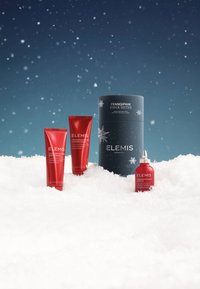 Rode tubes met lichaamscrème en douchegel met witte tekst, naast een rode glazen fles en een donkerblauwe cilindrische doos met sneeuwvlokken ontwerpen.
