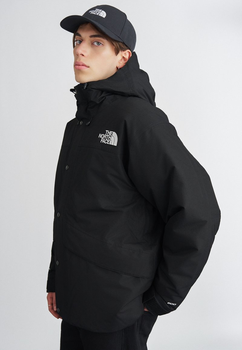 Crna izolirana jakna s visokim ovratnikom, zatvaračem i kopčama na dugmad, podesivim kapuljačom i logotipom The North Face na prsima i na kapi.