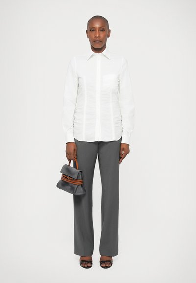 Camicia bianca con tessuto strutturato, pantaloni grigi su misura e una piccola borsa grigia con dettagli arancioni. Sandali neri con apertura sul davanti.