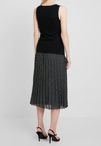 Černý tílko bez rukávů kombinované s černou a bílou puntíkovanou plisé sukní. Sukně má volný design a modelka má na sobě černé lodičky.