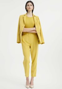 Żółty dopasowany garnitur z przylegającą marynarką i spodniami do kostek, wykonany z gładkiego materiału o klasycznym kroju i subtelnej połysku.