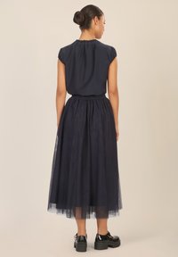 Top plisado azul marino de manga corta combinado con una falda de tul en capas hasta la rodilla; zapatos negros de suela gruesa.