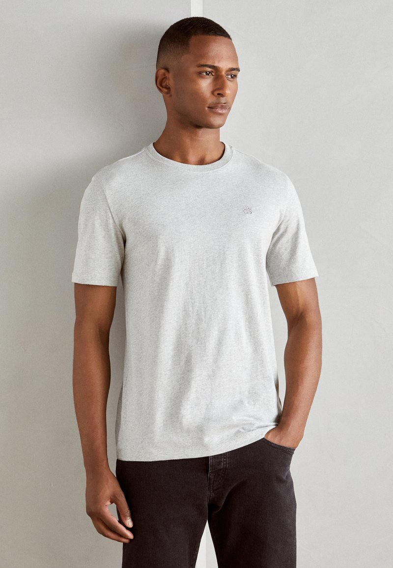 Grijs T-shirt met korte mouwen, gemaakt van zachte stof, met een ronde halslijn en een subtiele logodetail op de borst, gecombineerd met donkere broek.