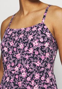 Blumenkleid mit dunkelblauem Hintergrund, das rosa und weiße Blumenmuster zeigt. Dünne Schulterträger und ein tailliertes Oberteil.