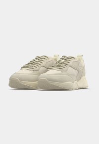 Pár béžových nízkych tenisek s hrubými podrážkami a textúrovanými detailmi, zobrazených z predného šikmého pohľadu na bielom pozadí.