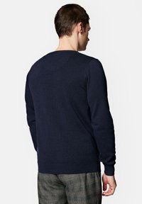 Granatowy sweter z długimi rękawami, okrągłym dekoltem, ściągaczami przy rękawach i u dołu, wykonany z miękkiego dzianinowego materiału. Noszony z wzorzystymi spodniami.