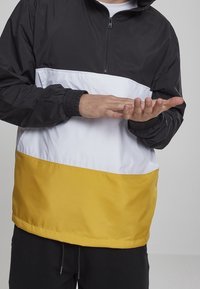 Kleurgeblokte windjack met een zwart bovenstuk, witte middelste sectie en gele ondersectie. Voorzien van een kwartrits en elastische manchetten.