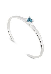 Brazalete de plata con un diseño sencillo, con una única piedra preciosa azul claro en el centro, acabado de superficie lisa y extremos abiertos.