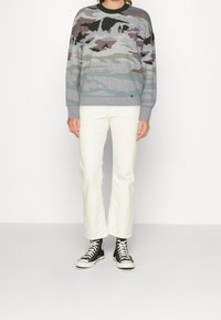 Suéter en gris con patrón de camuflaje, hecho de tejido de punto. Combinado con pantalones acampanados blancos y zapatillas alta negras.
