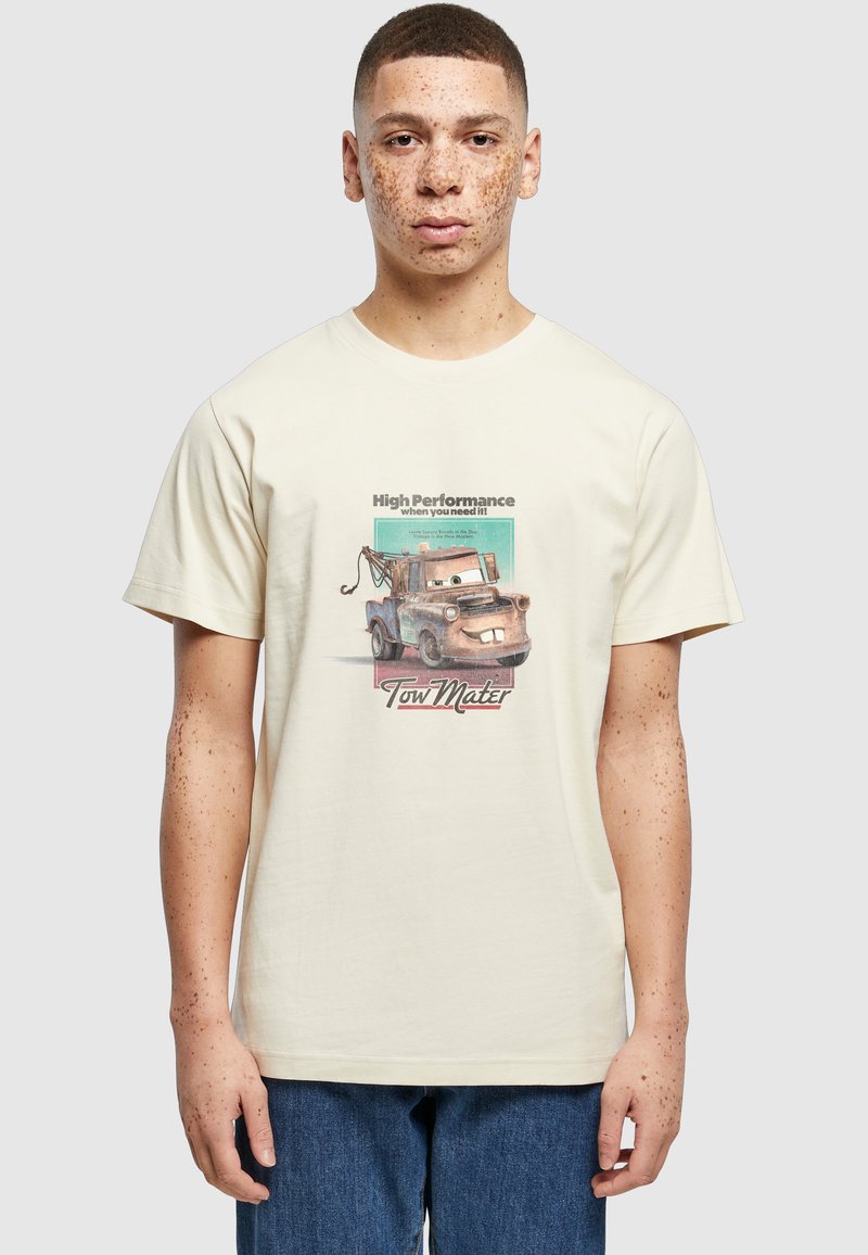 Jeune personne avec des taches de rousseur portant un t-shirt blanc avec un dessin animé de dépanneuse et les textes « High Performance » et « Tow Mater ».