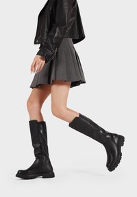 Stivali alti neri in pelle con una finitura testurizzata, dotati di una cerniera laterale e suole in gomma spessa per una buona aderenza.