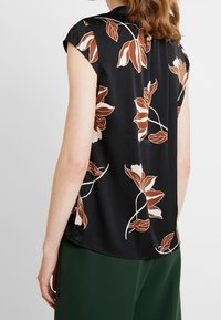 Sort blomsterbluse med korte ærmer, der har beige og rustfarvede blomsterdesigns. Glat stof med en let løs silhuet.