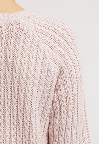 Ljusrosa stickad tröja med ribbad textur, med rund hals och raglanärmar.