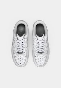 White leather sneakers with round toe, perforated toe box, contrasting grey inner lining, and flat white laces. Features subtle branding.