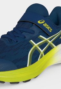 Σκούρο μπλε αθλητικό παπούτσι Asics με κίτρινη σόλα, λευκή και κίτρινη σχεδίαση με λωρίδες, μπλε κορδόνια και λουράκι με βέλκρο και κίτρινο λογότυπο Asics.