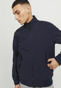 Chaqueta ligera de color azul marino con cuello alto, cierre de cremallera, bolsillos laterales y puños acanalados. Fabricada con un tejido suave y texturizado.