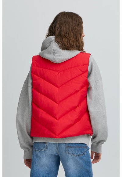 Červená puff vest s chevron prešívaním, pod ňou mäkká sivá mikina s kapucňou a džínsy. Zadný pohľad zvýrazňuje dizajn a farebný kontrast.