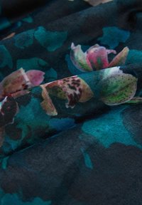 Dark fabric with a teal and green abstract floral pattern, featuring pink and white flower details and soft folds.