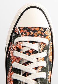 Baskets avec un motif floral orange et vert, en toile, embout en caoutchouc blanc, et lacets beiges. Accents noirs présents.