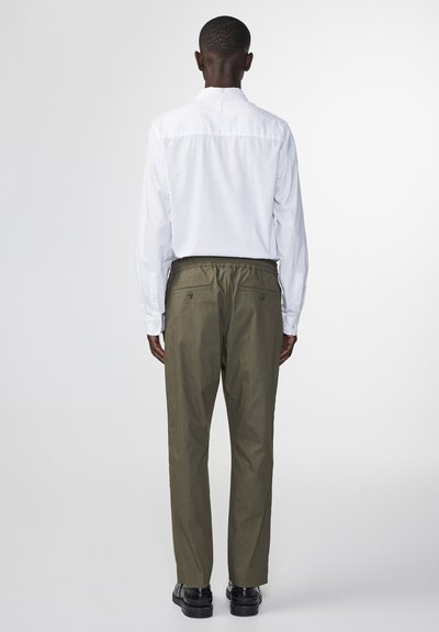 Chemise blanche à manches longues associée à un pantalon vert olive. Le pantalon est doté d'une taille élastique et de poches arrière. Texture de tissu lisse.