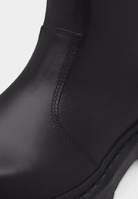 Κοντινό πλάνο μαύρης δερμάτινης μπότας που δείχνει λείο υλικό, λεπτομερή ραφές και μέρος του παχέος, ραβδωτού πέλματος.