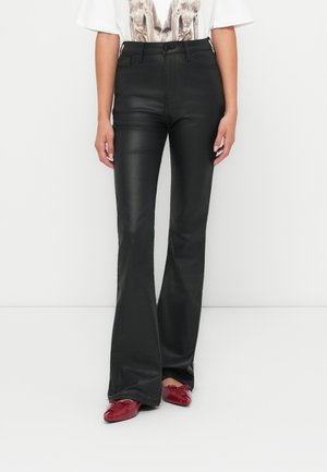 Pantaloni a zampa neri in similpelle con una texture liscia e vita alta, abbinati a scarpe rosse lucide.