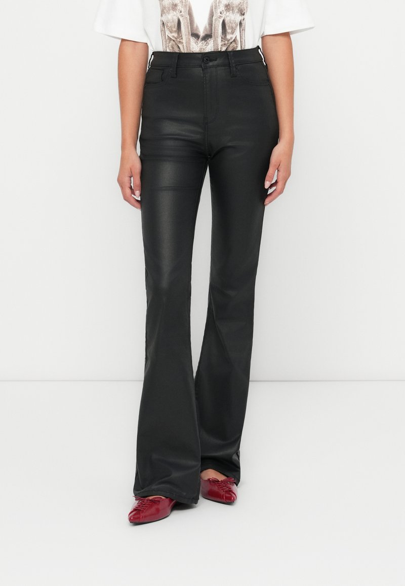 Zwarte flared broek van faux leer met een gladde textuur en hoge taille, gecombineerd met glanzende rode schoenen.
