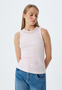 Helles rosa, geripptes Tanktop mit rundem Ausschnitt, das eine dekorative Perlenakzent am Kragen trägt. Kombiniert mit blauen Jeans.