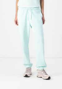 Licht mintgroene sweatpants met een trekkoord in de taille, ribbelmanchetten en een zachte textuur, gecombineerd met grijze en zwarte sport schoenen.