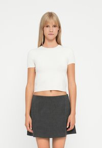 Tricou alb, scurt, cu mâneci scurte, asociat cu o fust�ă gri cu carouri. Design simplu, textură netedă și formă ajustată.