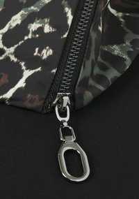 Tissu à motif noir et vert avec une tirette de fermeture éclair en métal. La fermeture éclair est argentée avec un attachement rectangulaire. Texture lisse avec un design vif.