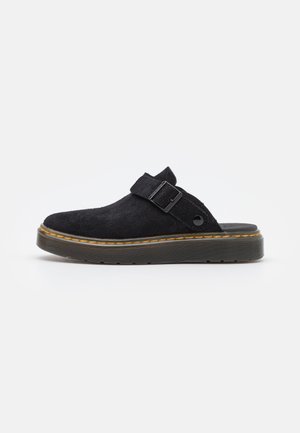 Scarpa slip-on nera in suede con suola platform spessa, dotata di una singola cinghia e una fibbia. Accentuata da cuciture gialle lungo la suola.