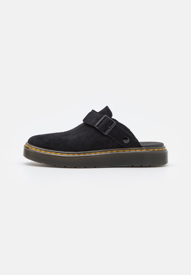 Scarpa slip-on nera in suede con suola platform spessa, dotata di una singola cinghia e una fibbia. Accentuata da cuciture gialle lungo la suola.
