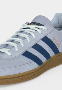 Baskets Adidas gris clair avec des bandes bleues, des lacets blancs, une semelle en gomme et « Spezial » imprimé en doré sur le panneau latéral.
