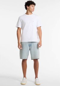 Valge puuvillane taskuga t-särk, kombineeritud helesiniste teksapükstega. Modelli jalas valged tossud, seisab neutraalsel taustal.